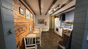 Un estrecho pasillo con paredes de madera, un comedor con mesa y sillas, una cocina con electrodomésticos y un extintor de incendios en la pared.