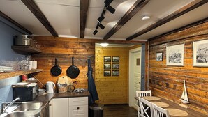 Una cocina con paredes de madera, un comedor con mesa y sillas, y una puerta que da a otra habitación.