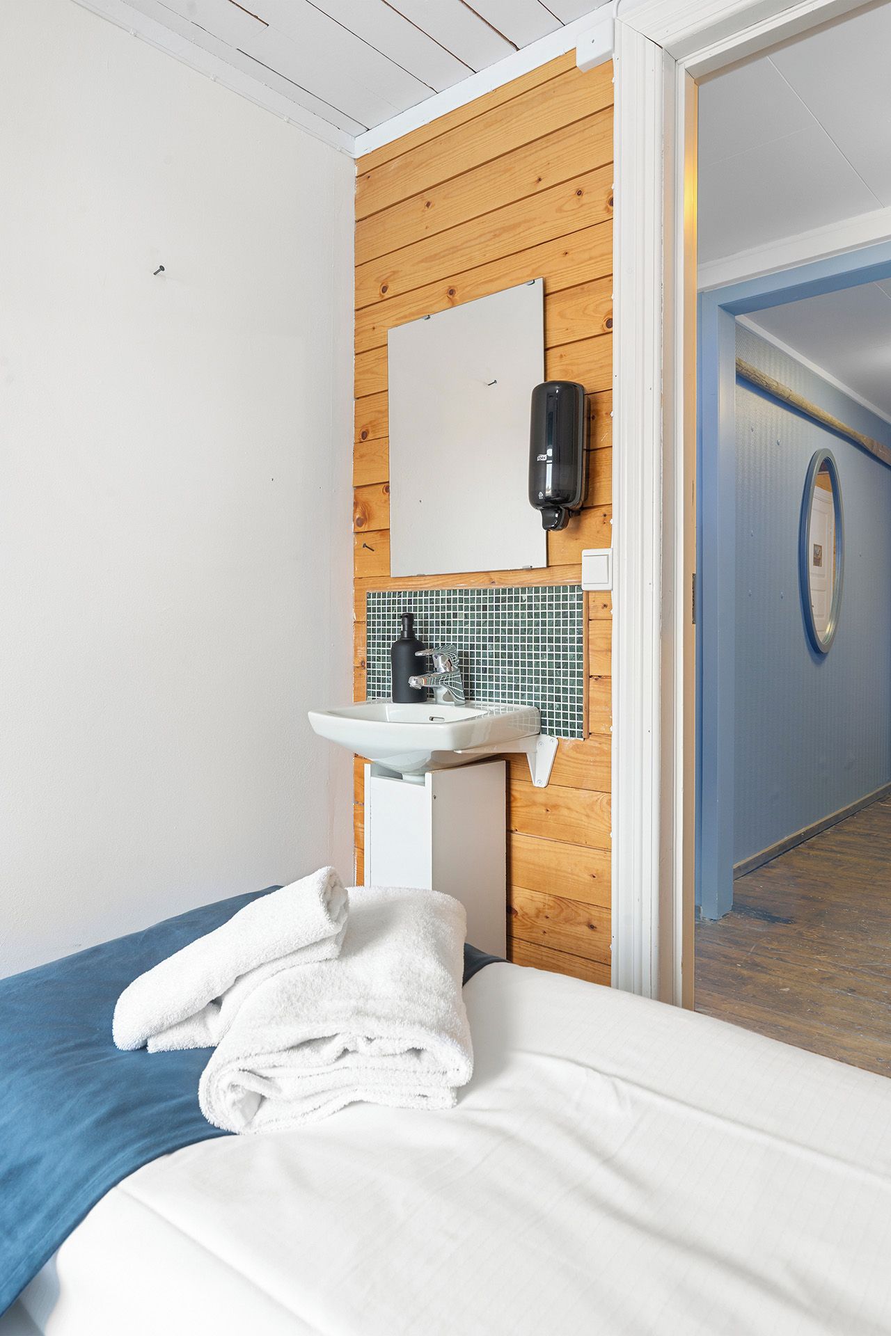 Ett hotellrum med en säng, ett handfat, en spegel och en dörr som leder ut till en korridor.