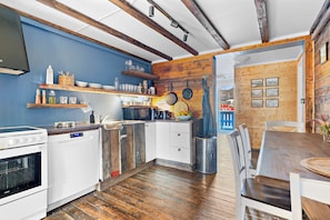 A kitchen with wooden beams, a stove, and a dining area with a table and chairs. - Astra Whale - Waterfront Boutique Hostel in Lofoten (Vagan)
