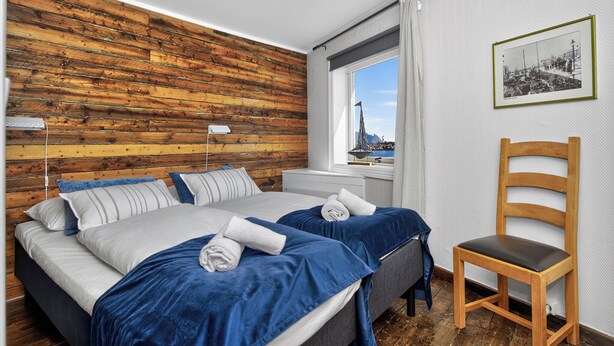 Un dormitorio con pared de madera, una cama con ropa de cama azul, una silla y una ventana con vistas.