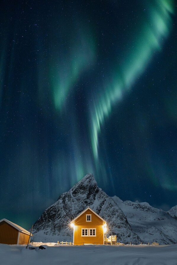 A snow-covered mountain with a wooden cabin illuminated by warm lights.