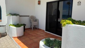 A covered patio area with potted plants, a chair, and a sliding glass door. - Paradise Villa #5 | Oceanfront Escape at Playa Encanto (Puerto Peñasco)