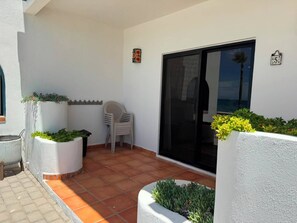 A covered patio area with potted plants, a chair, and a sliding glass door. - Paradise Villa #5 | Oceanfront Escape at Playa Encanto (Puerto Peñasco)