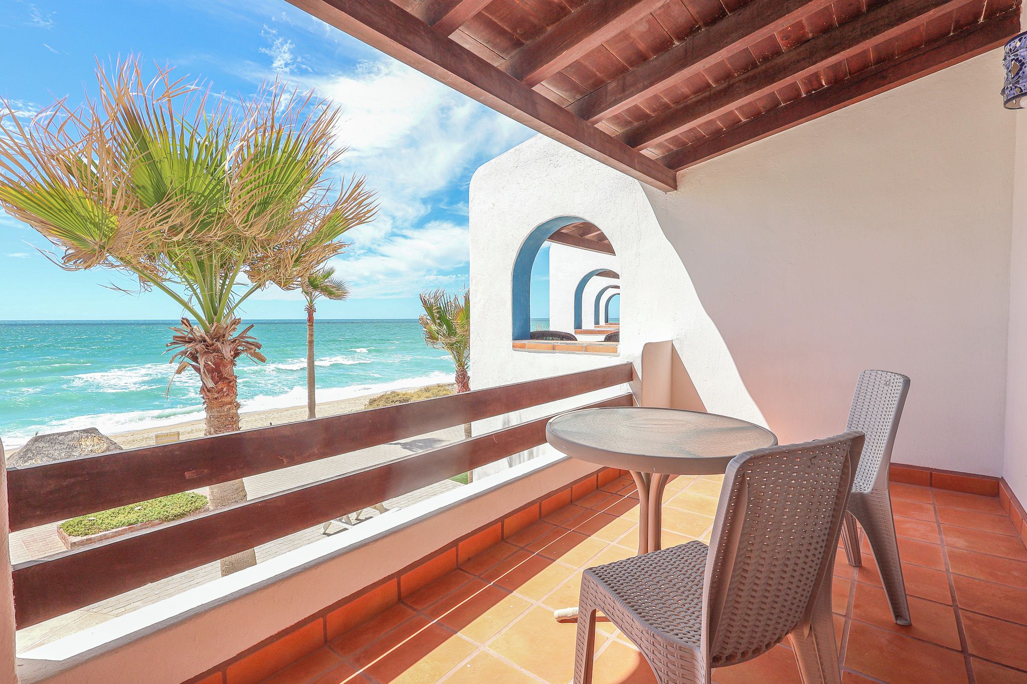 A balcony with a view of the ocean, a table, two chairs, and a wooden railing.