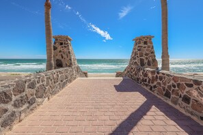 A paved pathway leading to the beach with stone walls on either side and palm trees. - Paradise Villa #5 | Oceanfront Escape at Playa Encanto (Puerto Peñasco)