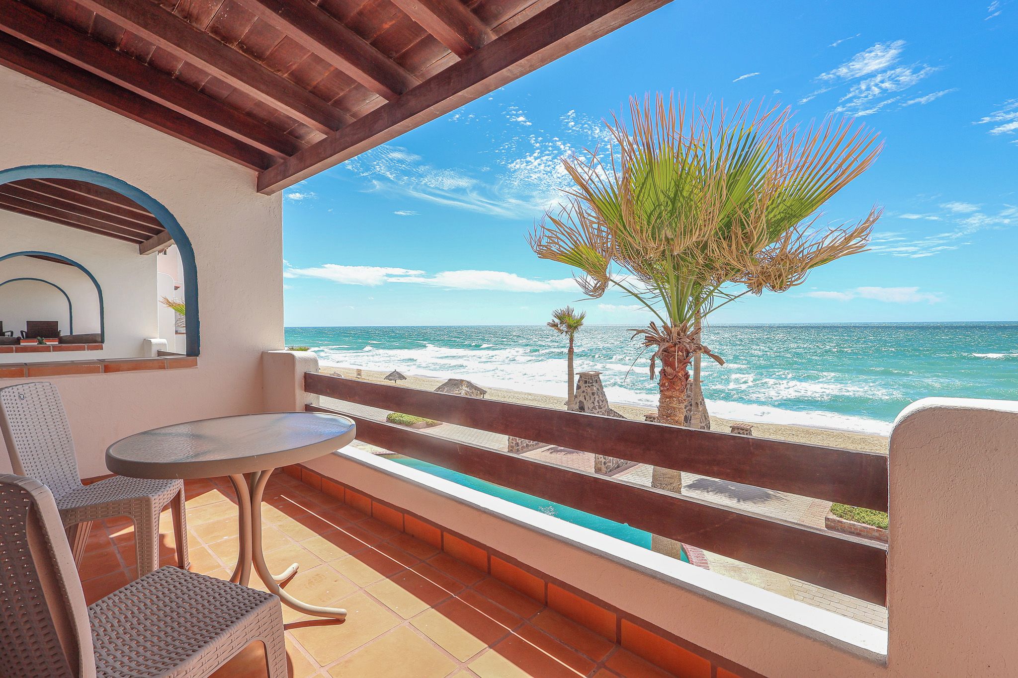 Un balcone con vista sull'oceano, un tavolo, sedie e una palma.