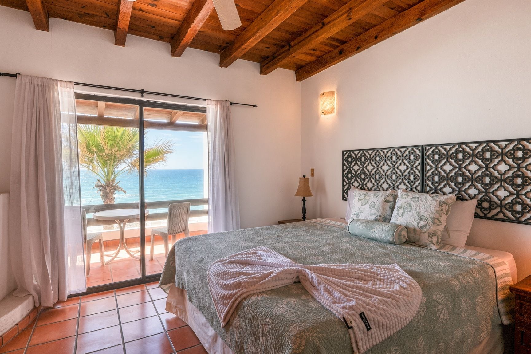 Un dormitorio con una cama grande, vistas al océano, un balcón con una silla y un cabecero estampado.