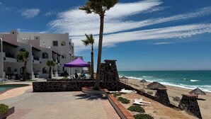 A beachfront hotel with a pool, a stone wall, and a beach area with umbrellas. - Paradise Villa #5 | Oceanfront Escape at Playa Encanto (Puerto Peñasco)