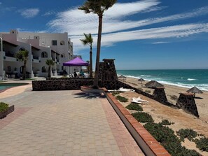 A beachfront hotel with a pool, a stone wall, and a beach area with umbrellas. - Paradise Villa #5 | Oceanfront Escape at Playa Encanto (Puerto Peñasco)