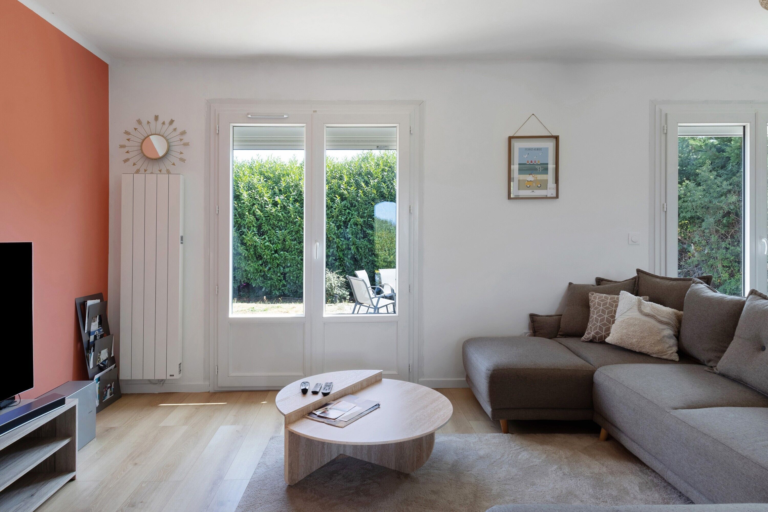 Een moderne woonkamer met een bank, een salontafel en een televisie. Twee schuifdeuren leiden naar een tuin.
