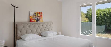 A bedroom with a large bed, a bedside table, a floor lamp, and a window with a view of greenery.