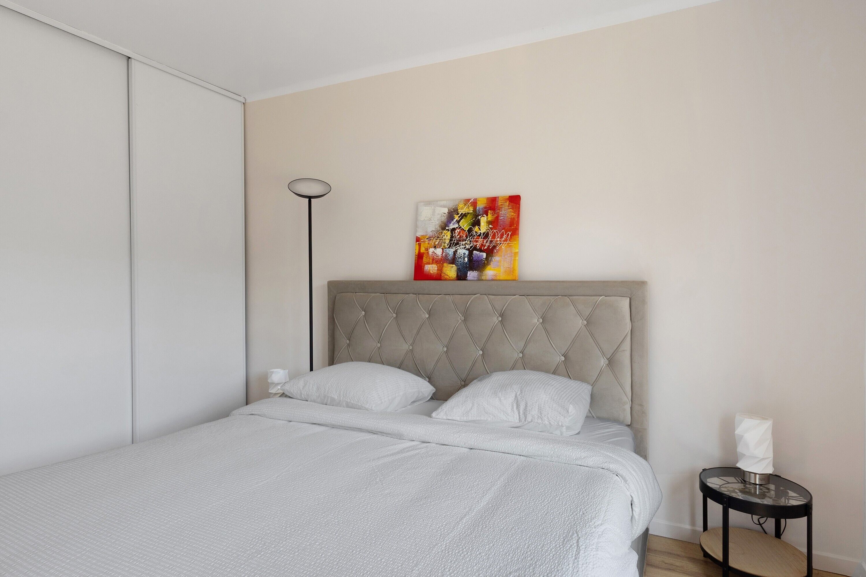 Ein Schlafzimmer mit einem Bett, einem Nachttisch, einer Stehlampe und einem Gemälde an der Wand.