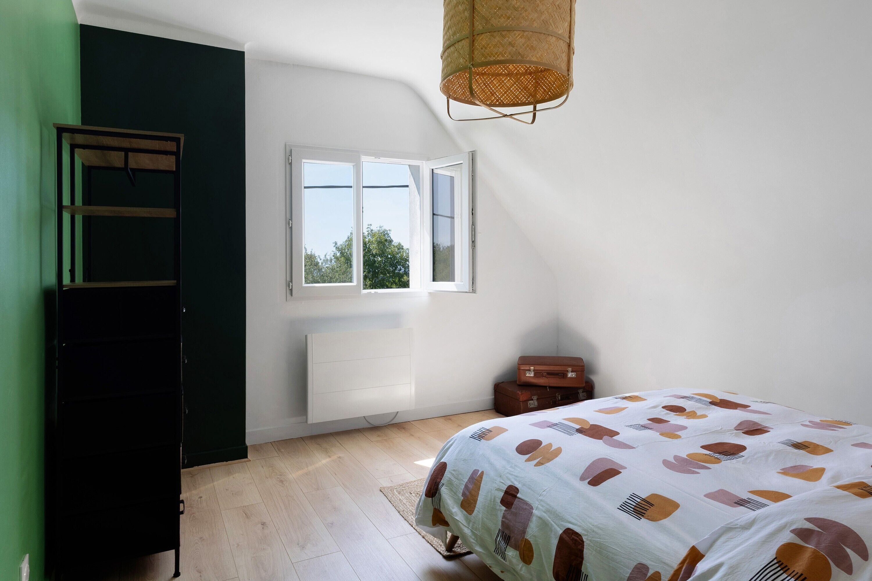 Een slaapkamer met een bed, een raam, een radiator, een kledingkast en een hanglamp.
