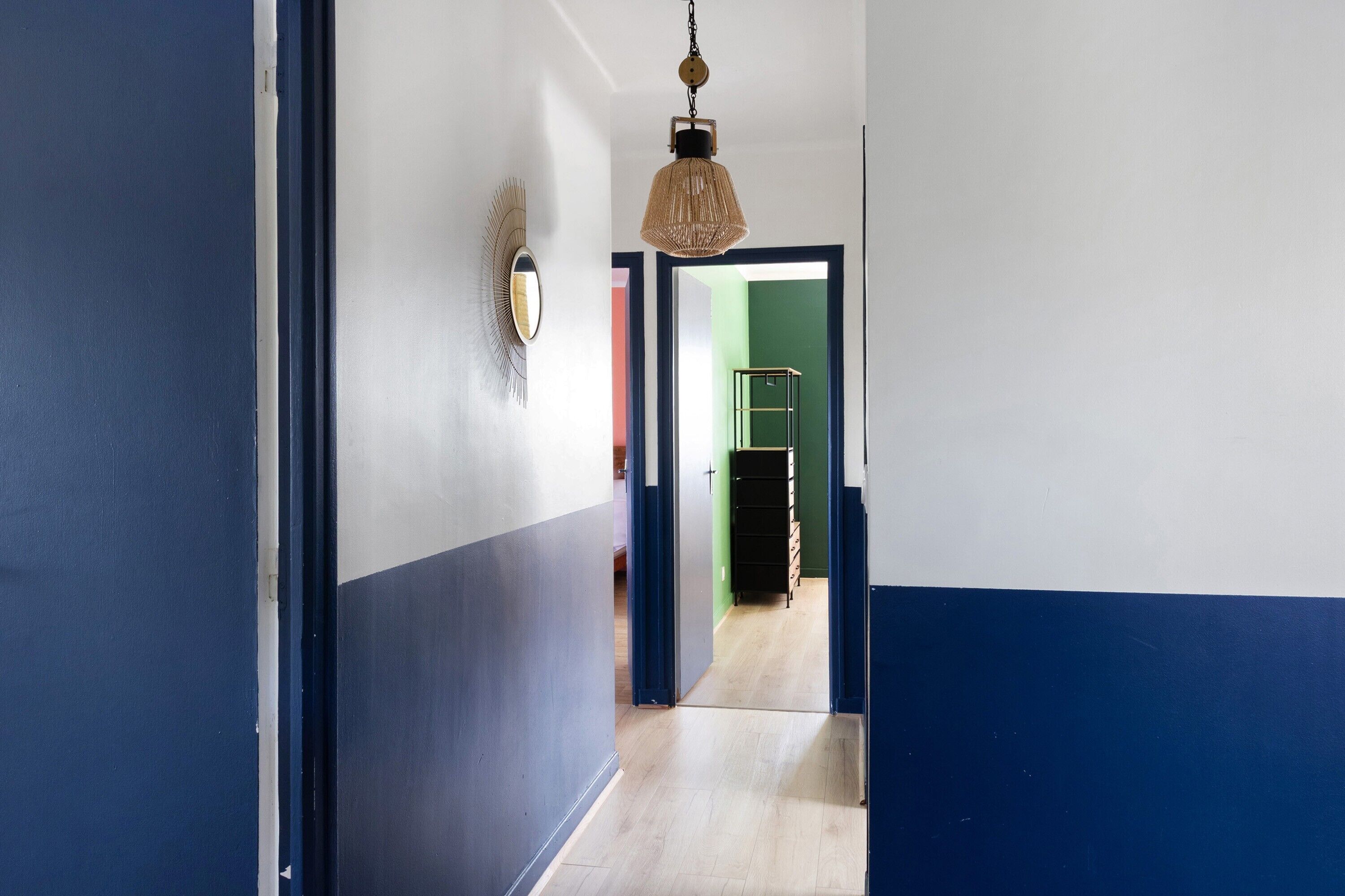 Ein Flur mit blauer und weißer Wand, einer hängenden Leuchte und einer Tür zu einem anderen Raum.