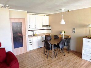 Eine kleine Küche mit weißen Schränken, einer Holzarbeitsplatte und einem Essbereich mit Tisch und Stühlen.