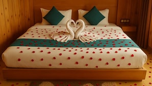 Una cama con una disposición de toallas en forma de corazón, una colcha verde azulado y lunares rojos.