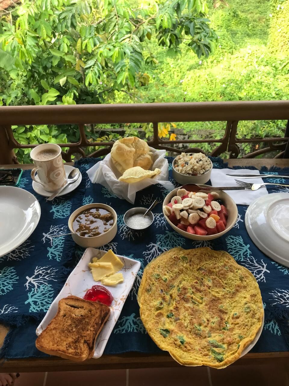 Una mesa al aire libre con diversos alimentos, incluyendo pan, un cuenco de fruta y una tostada.