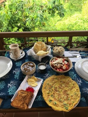 A table set outdoors with a variety of food items including bread, a bowl of fruit, and a plate of toast. - Mandaram villas (Mararikulam)