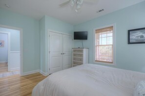 A bedroom with a bed, a television on the wall, a wardrobe, and a window with blinds. - OKI Hideaway: Ocean Views, Pool, Walk to Beach, Dog Friendly, Sleeps 7 (Oak Island)