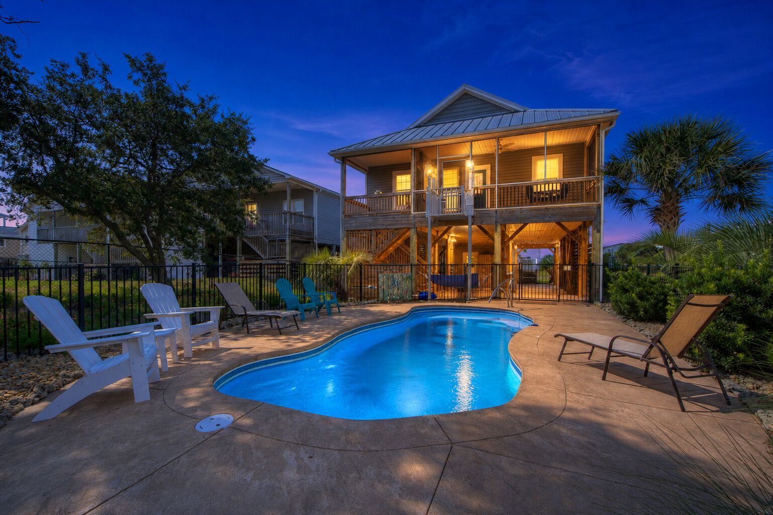 A two-story house with a swimming pool, outdoor seating, and a fenced yard.