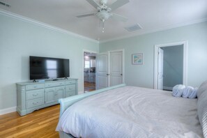 Une chambre à coucher comprenant un lit, un téléviseur, une commode et un ventilateur de plafond.