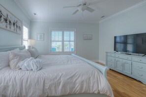 Ein Schlafzimmer mit einem Bett, einem Fernseher, einem Deckenventilator und einem Fenster mit Jalousien.
