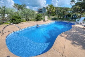 A swimming pool with a curved edge, surrounded by a concrete deck and a metal fence. - OKI Hideaway: Ocean Views, Pool, Walk to Beach, Dog Friendly, Sleeps 7 (Oak Island)