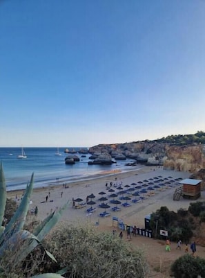 A beach with umbrellas, a lifeguard tower, and rocky cliffs. - Boho Guesthouse Portimão | A Slow Living Escape (Portimão)
