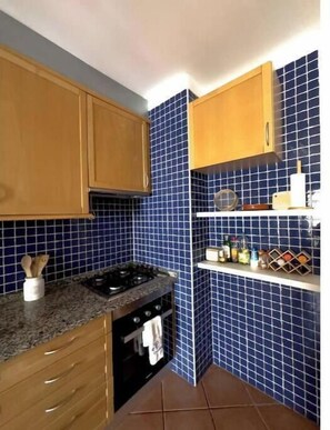 A kitchen with blue tiles, wooden cabinets, a stove, and a sink. - Boho Guesthouse Portimão | A Slow Living Escape (Portimão)