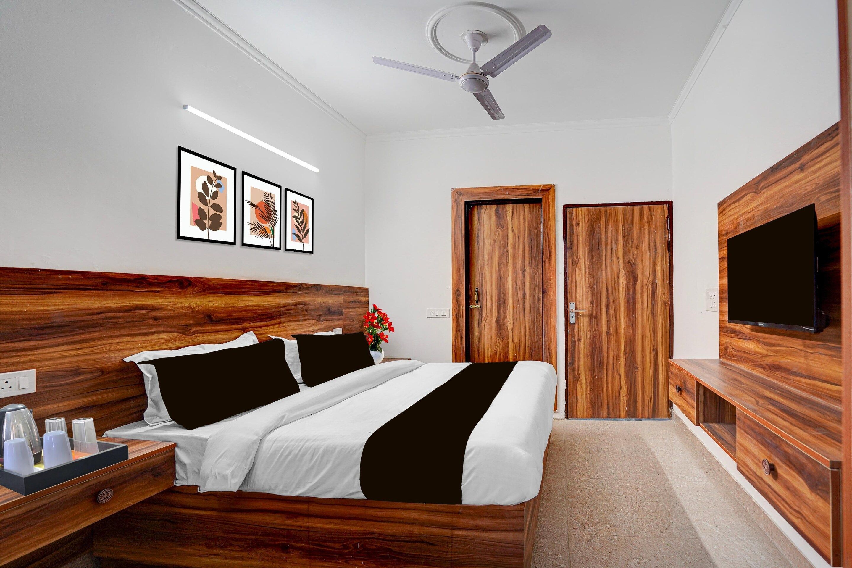 A modern bedroom with a wooden headboard, a bed with black and white bedding, a ceiling fan, a TV on the wall, and framed artwork on the wall.
