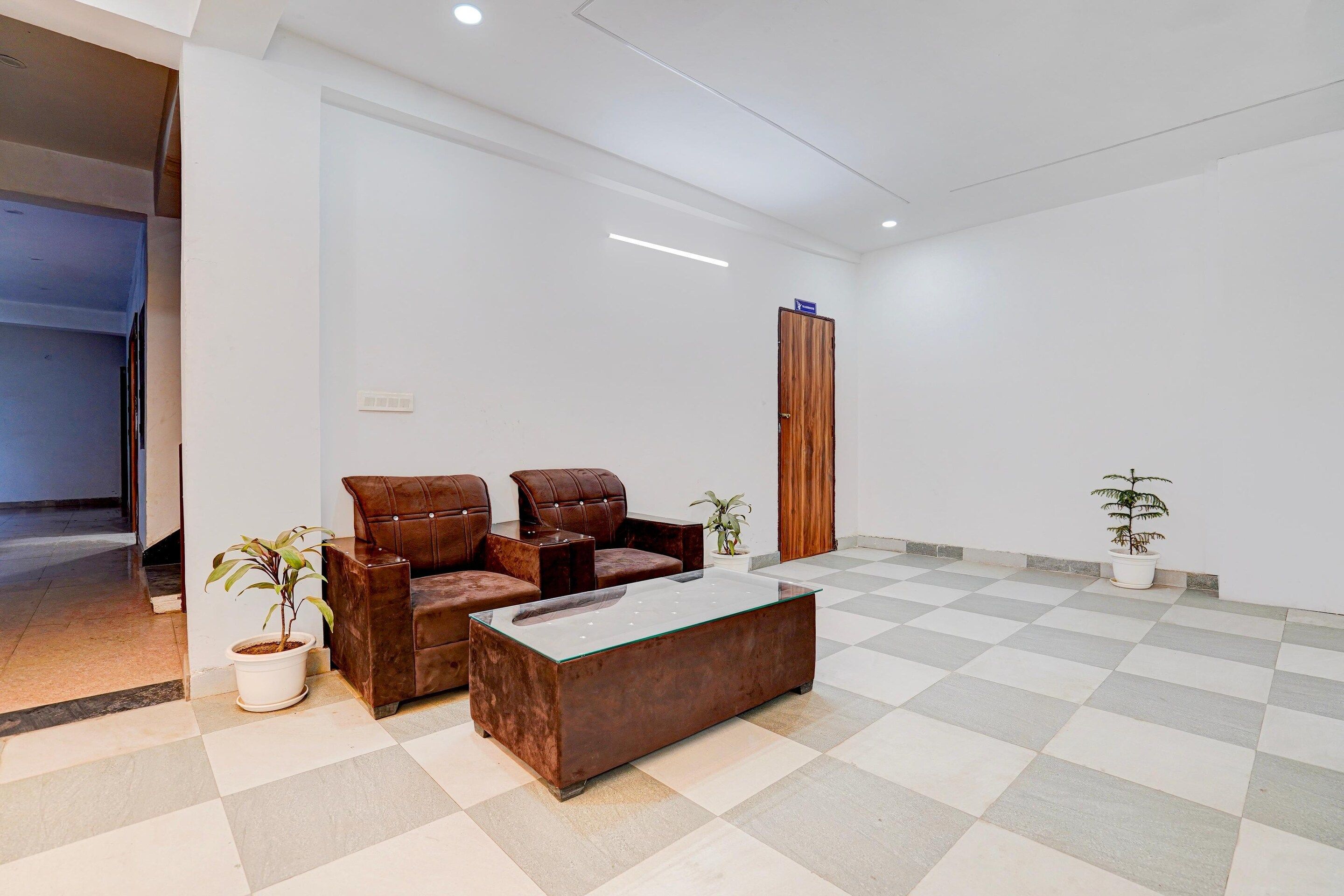A modern waiting area with a checkered floor, a brown leather sofa, a glass coffee table, and two potted plants.