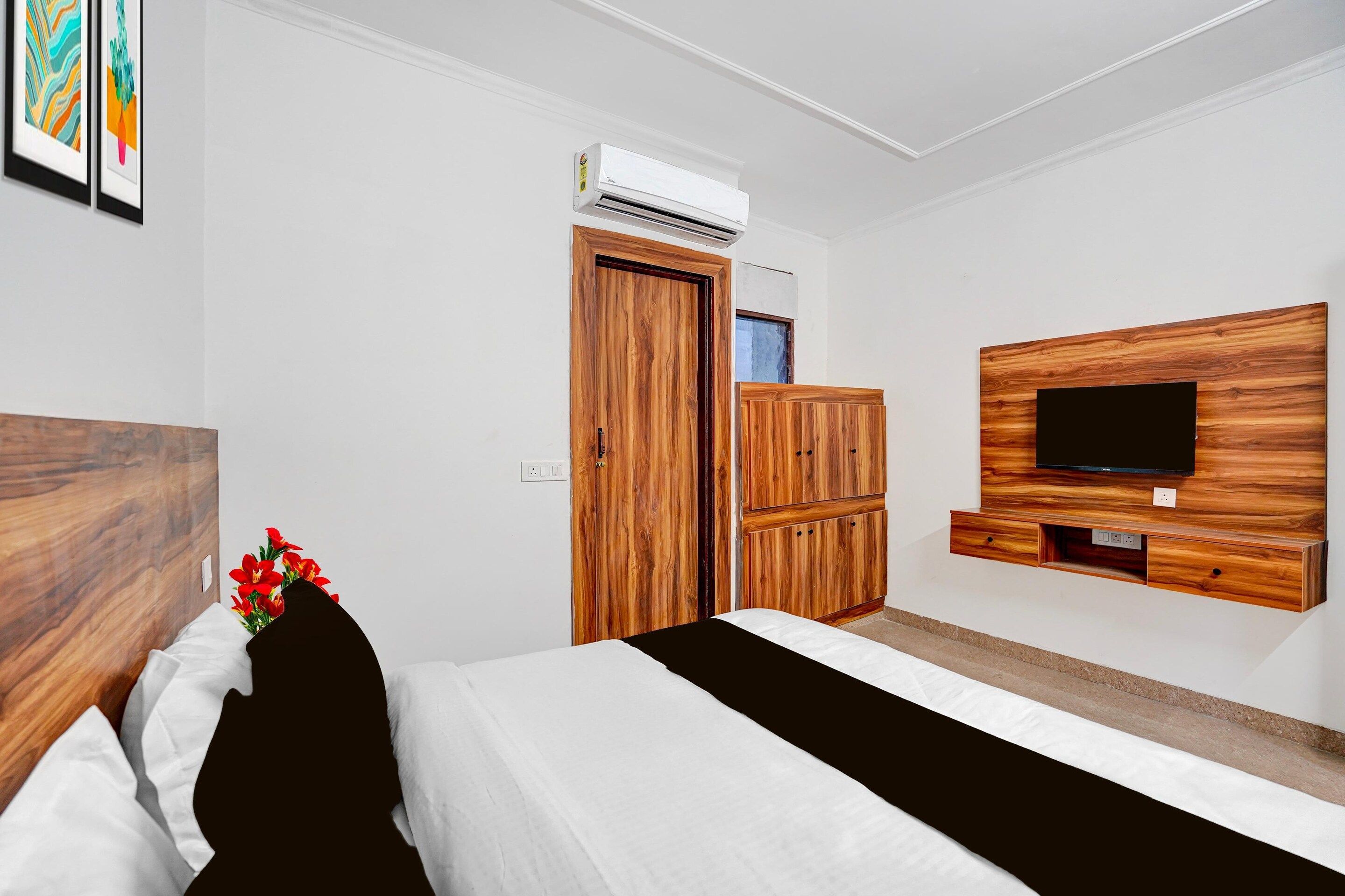 A hotel room with a bed, a wooden wardrobe, a television mounted on a wooden panel, and an air conditioning unit on the wall.