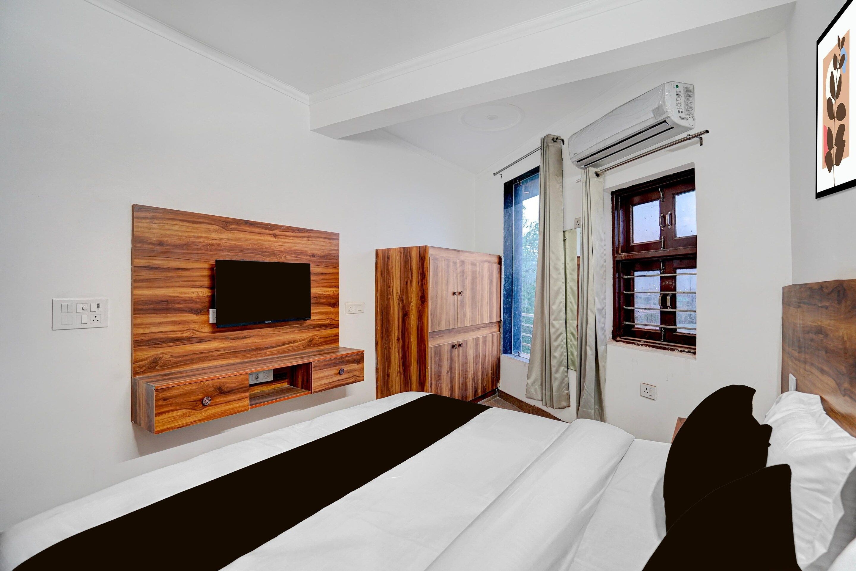 A bedroom with a bed, a TV mounted on a wooden panel, a wardrobe, and an air conditioning unit.