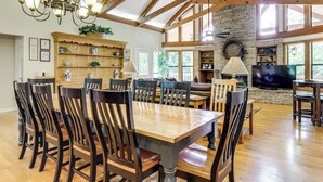 Een ruime eethoek met een grote houten tafel en stoelen, een kroonluchter en een stenen open haard.