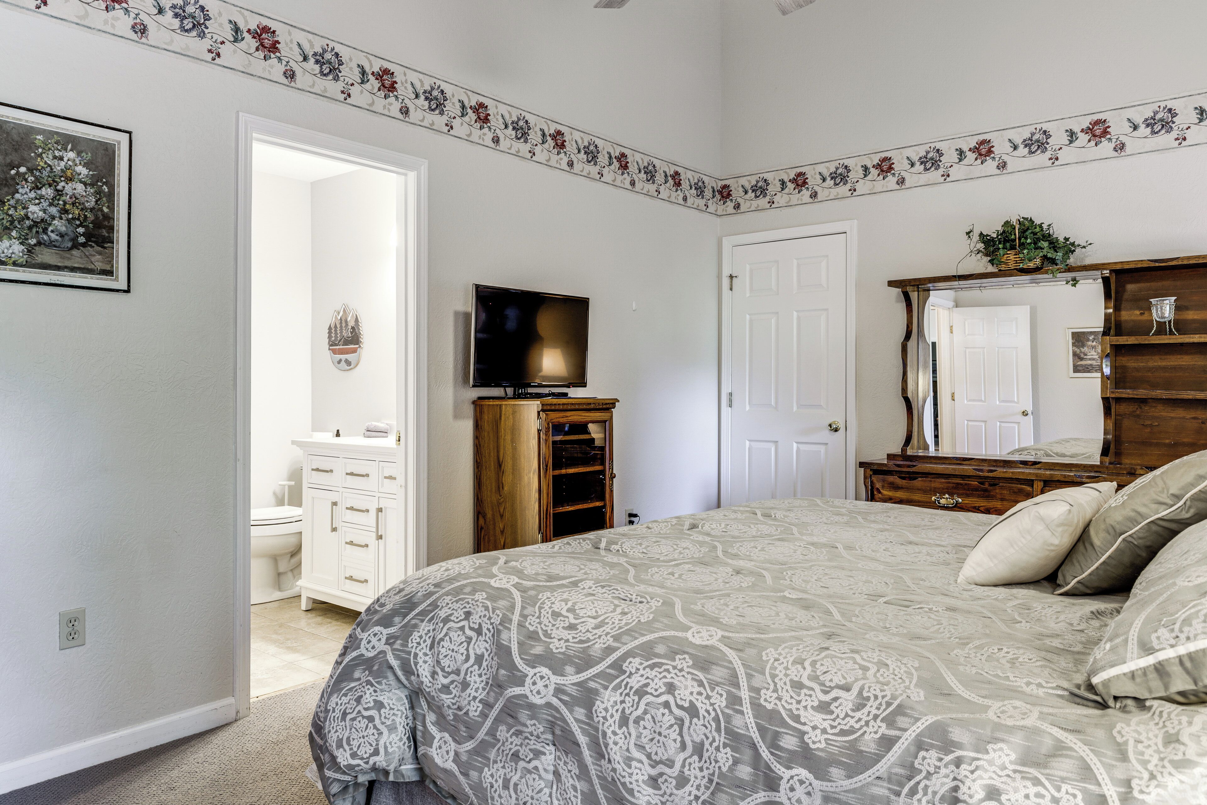Une chambre à coucher comprenant un lit, une commode, un téléviseur et une porte donnant accès à une salle de bain.