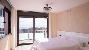 Ein Schlafzimmer mit einem großen Bett, einer Kristallleuchtre, einer Glasschiebetür zu einem Balkon und Blick auf die Landschaft.