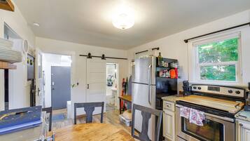 A kitchen with a wooden table, chairs, a refrigerator, a stove, and a window with a view of greenery.
