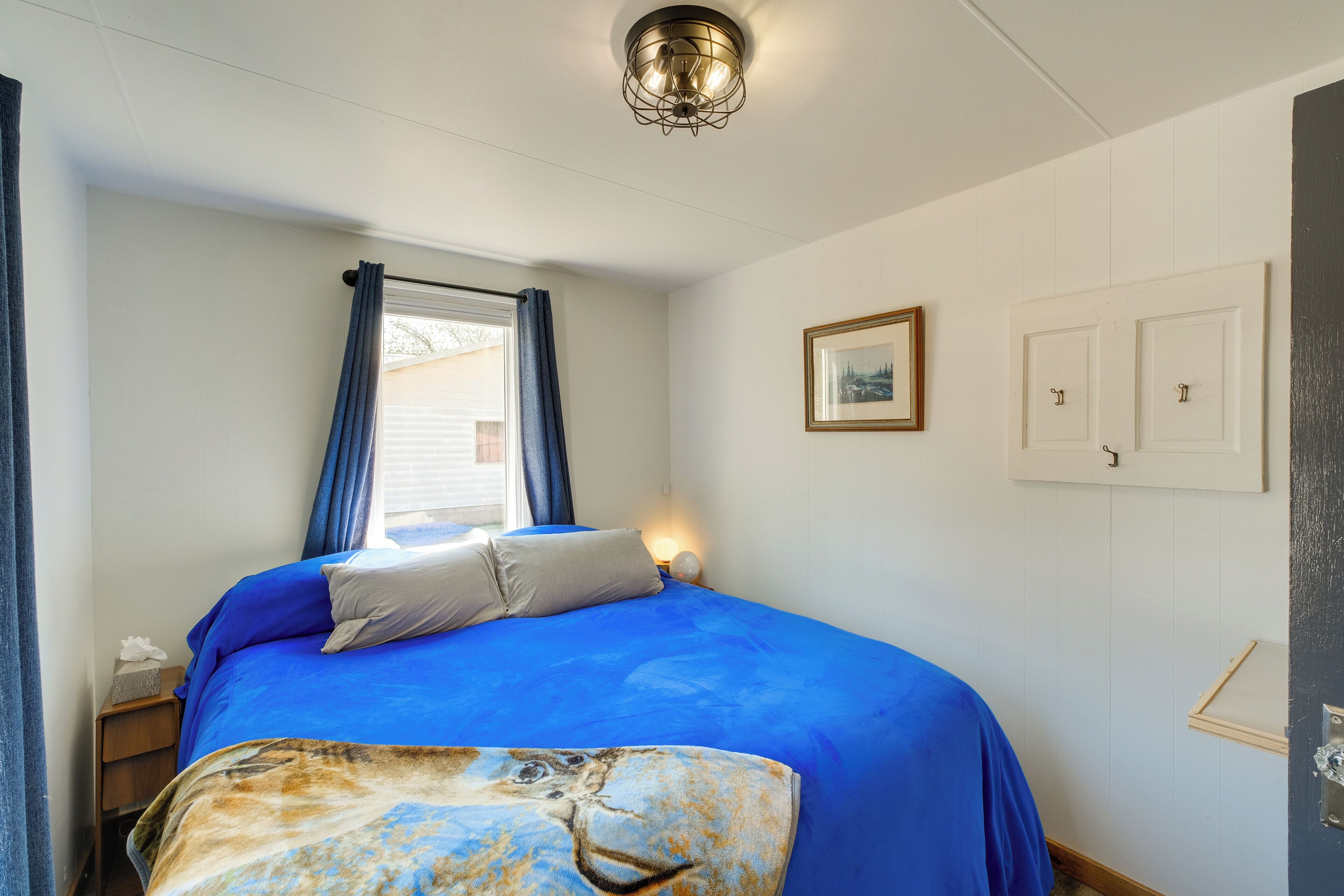 A bedroom with a bed, a window with curtains, a wall-mounted picture, and a door.