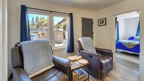 A room with two leather recliners, a small table with a tray and books, a bed with a blue cover, and a door leading to another room.