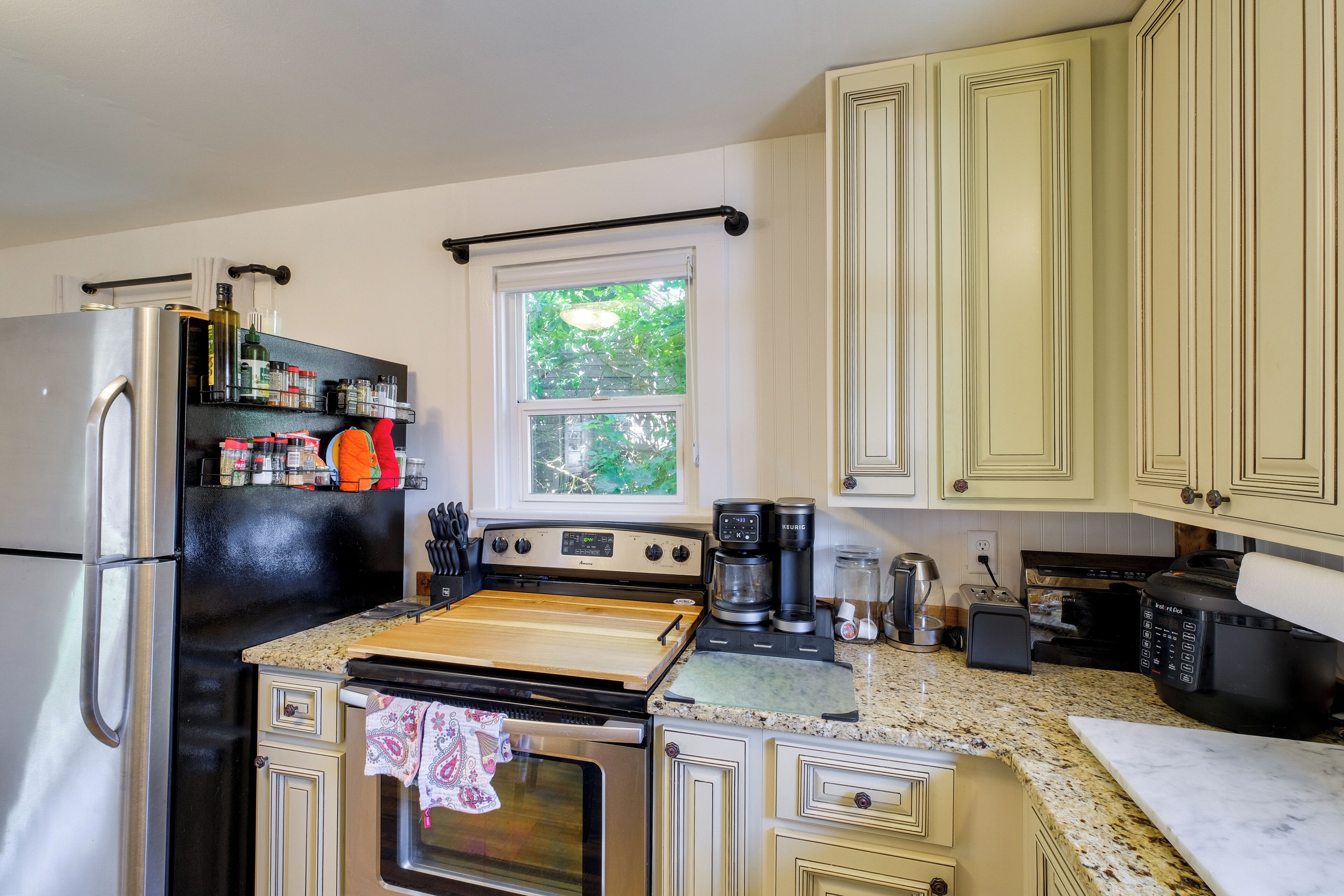 A kitchen with a refrigerator, stove, oven, and various appliances. There is a window with a view of greenery outside.