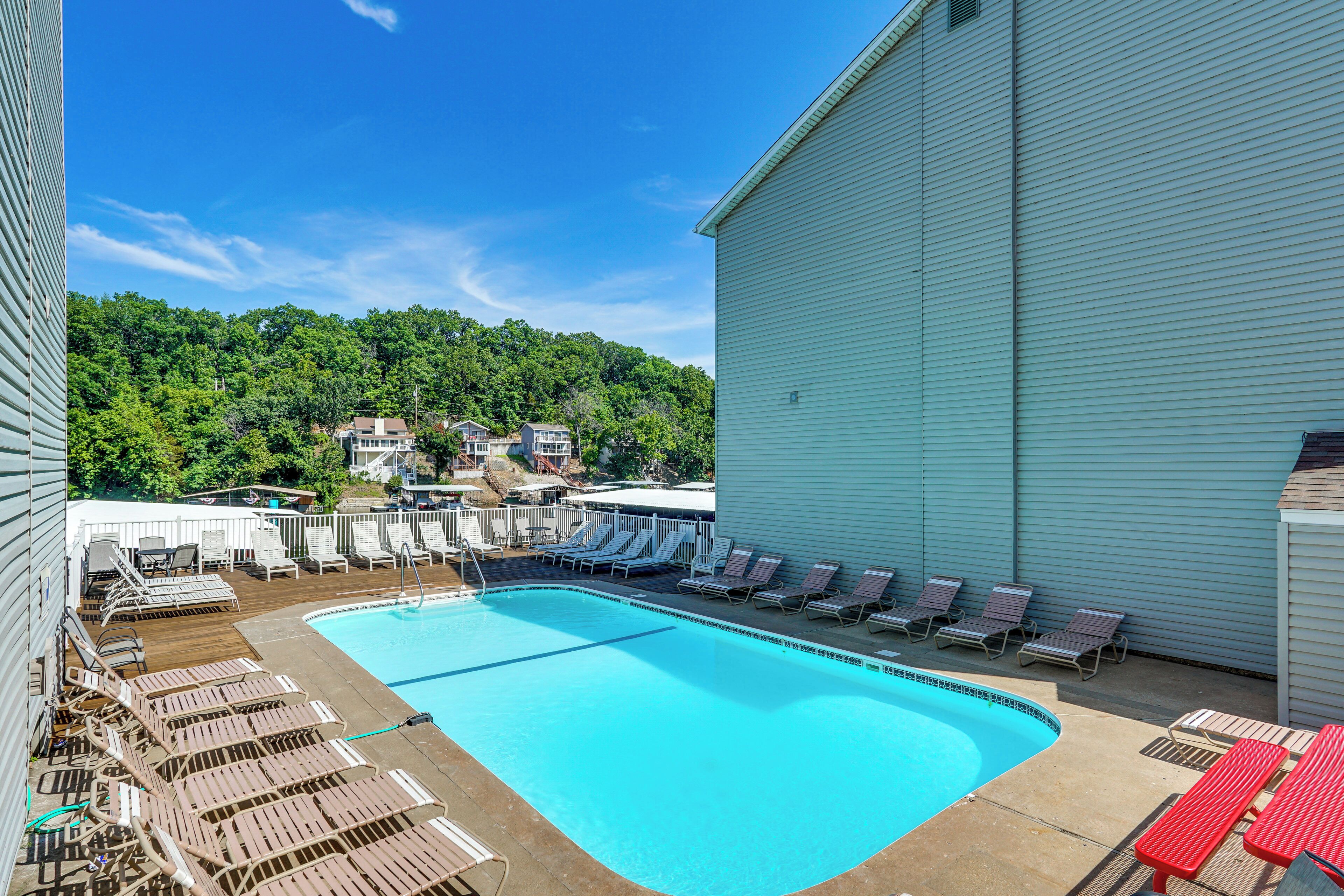 A swimming pool with lounge chairs, a deck area, and a view of a forested hillside.