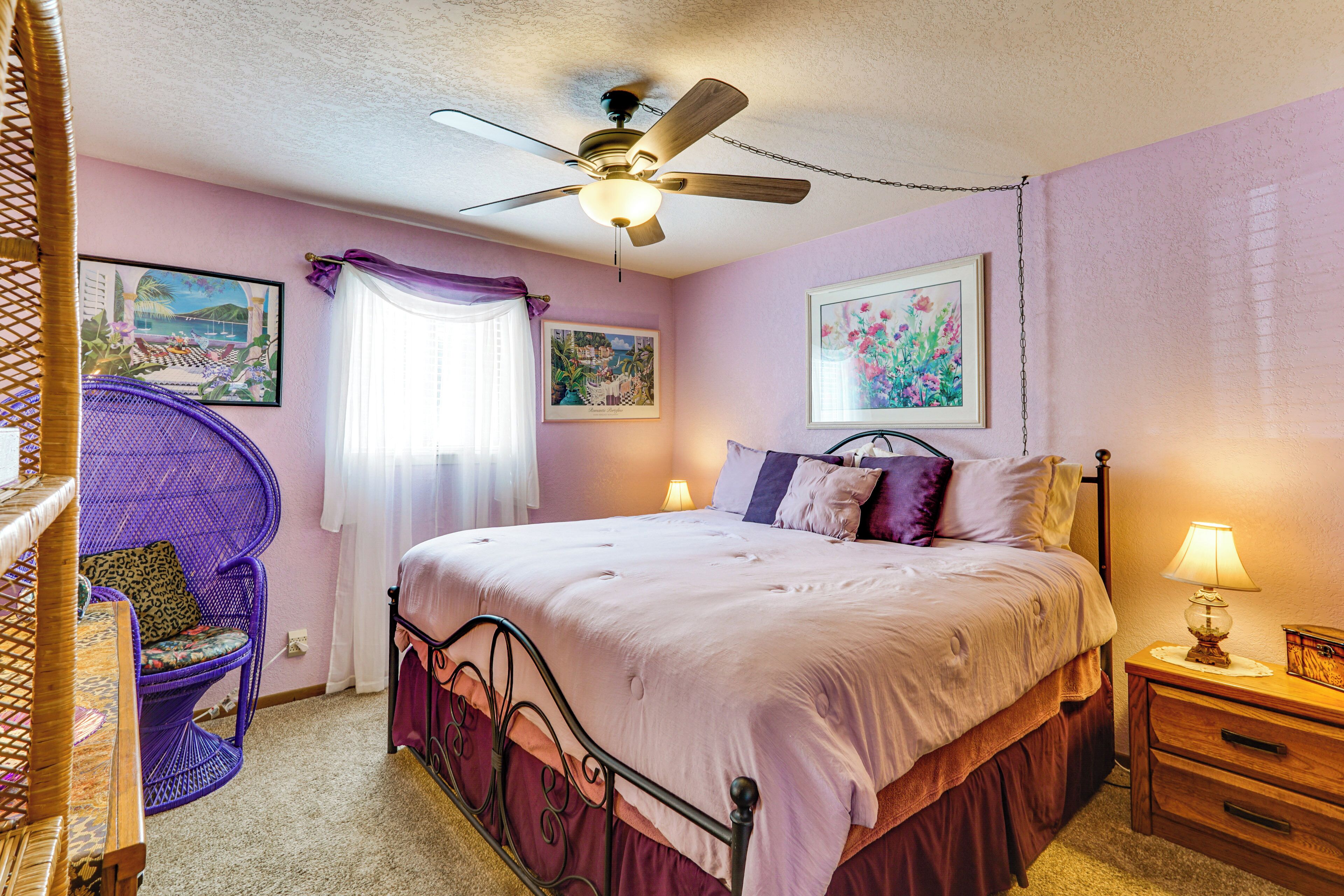 A bedroom with a bed, a chair, a nightstand, a lamp, and a ceiling fan.