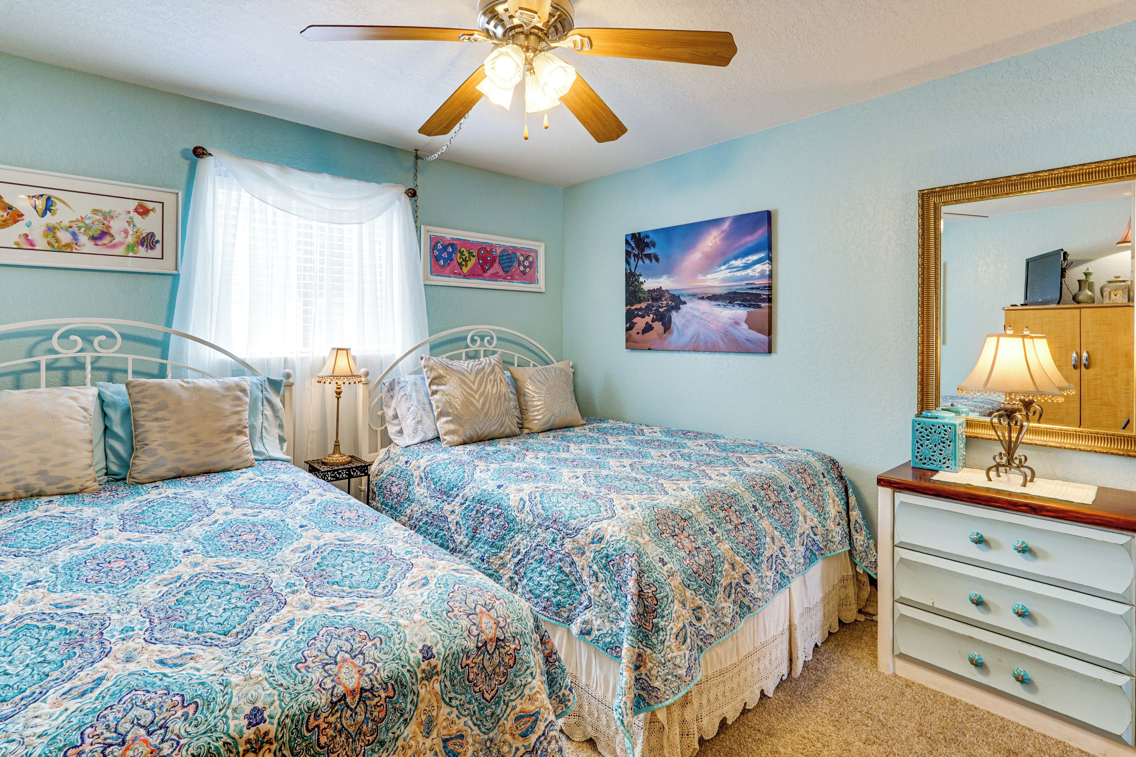 A bedroom with two beds, a ceiling fan, a dresser, and artwork on the walls.