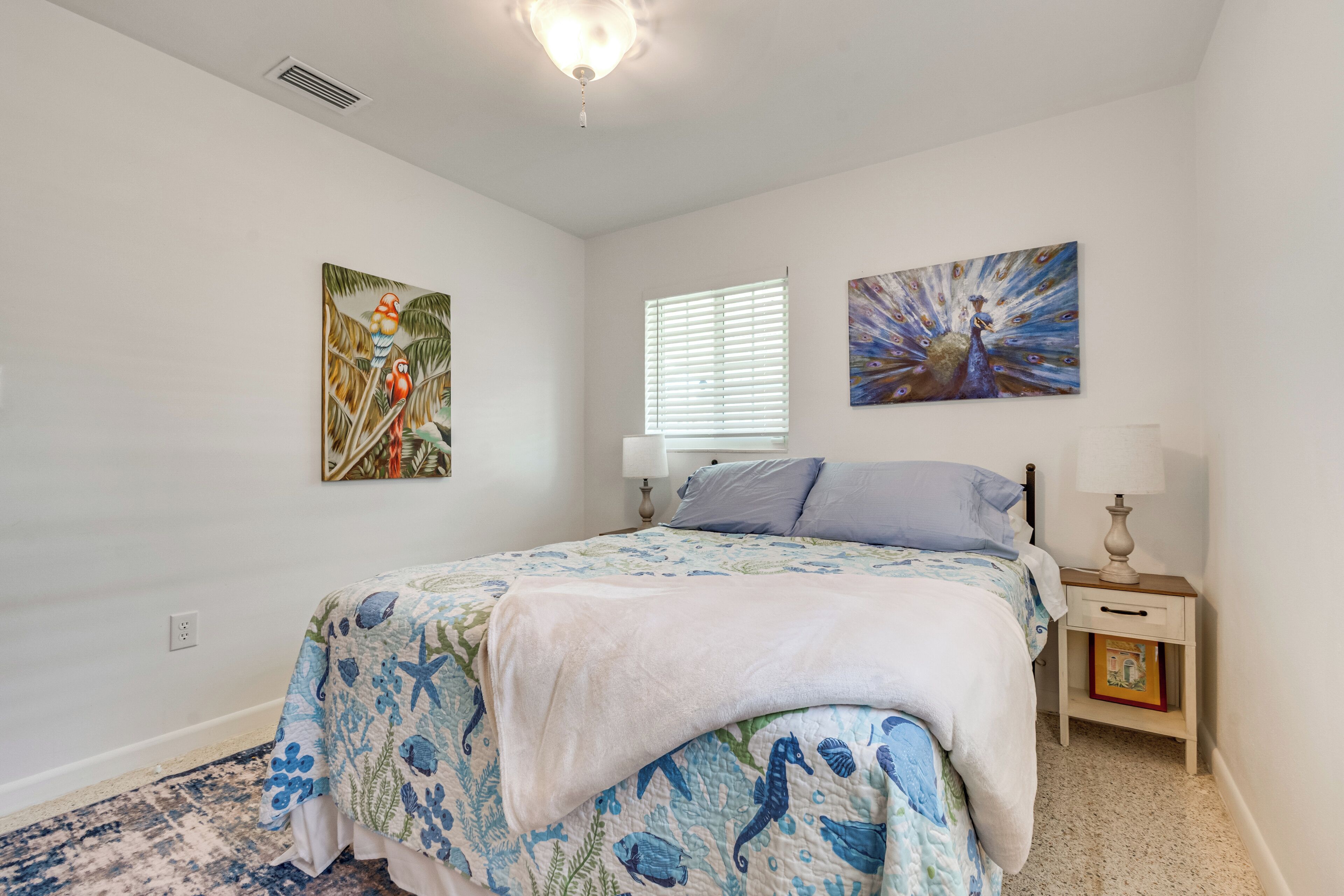 A bedroom with a bed, a nightstand, a lamp, and two wall-mounted paintings.