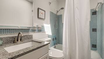 A bathroom with a sink, mirror, shower, and toilet.