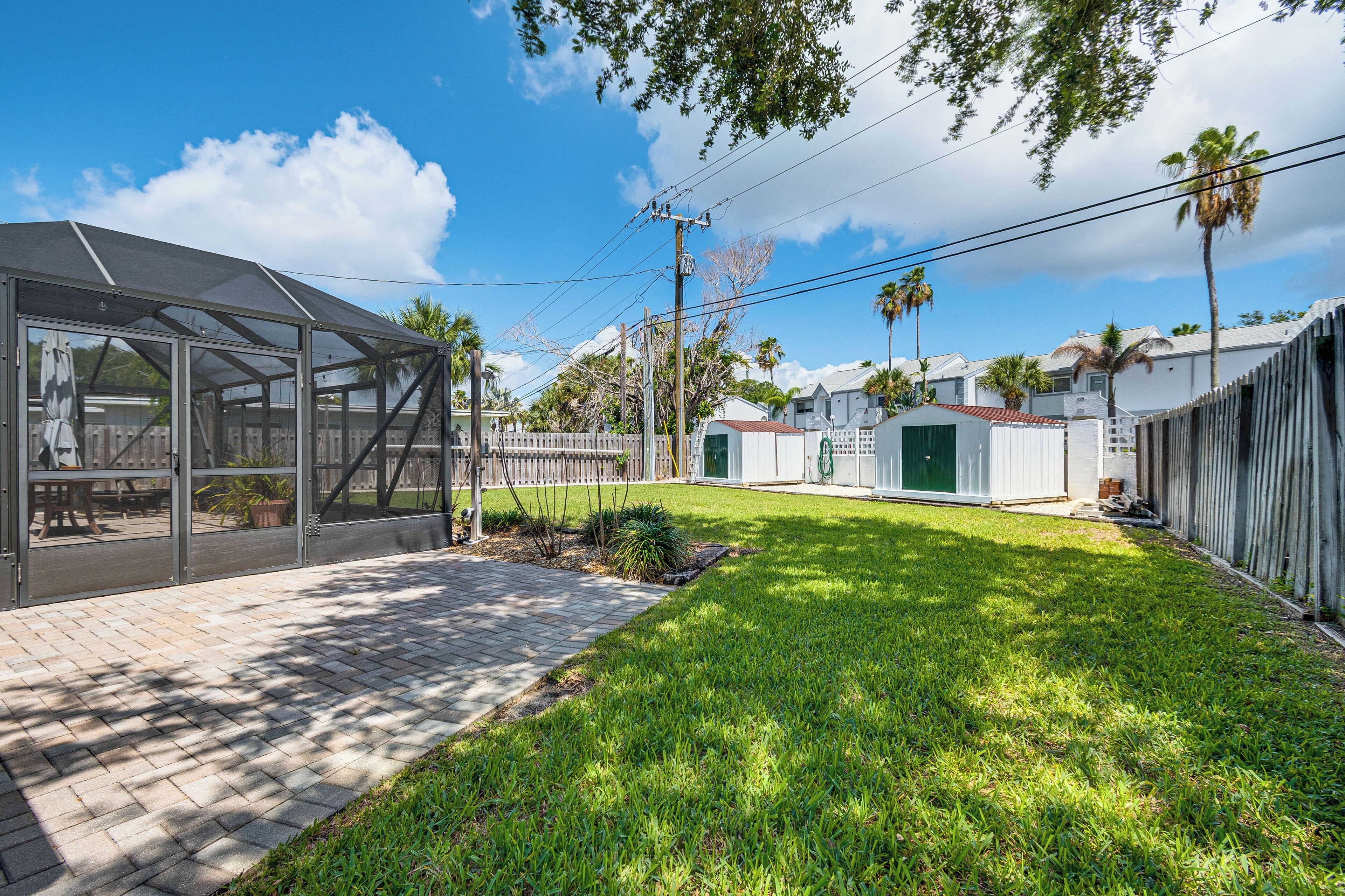 A backyard with a covered patio, a grassy lawn, and a wooden fence.