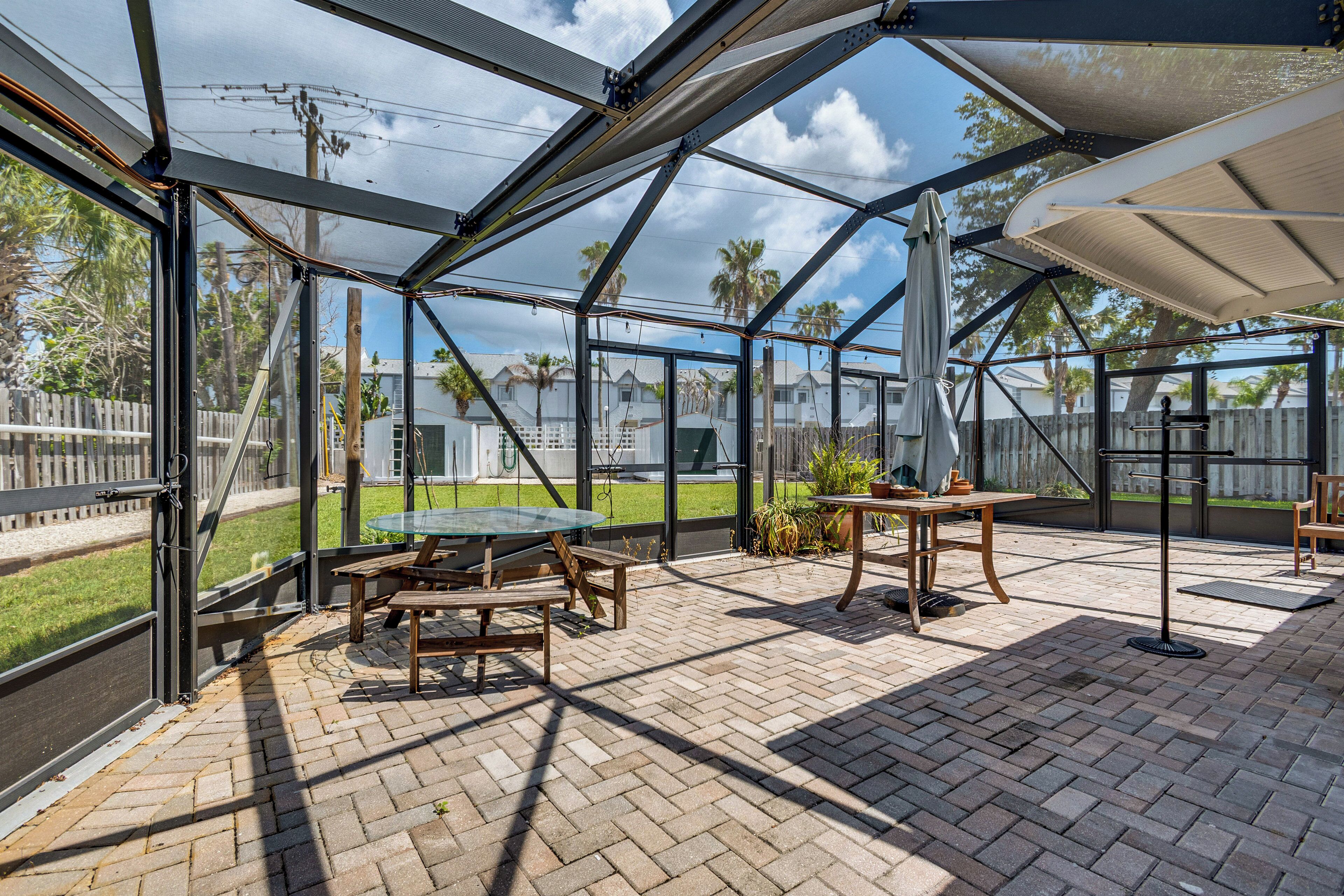 A covered patio with a brick floor, wooden furniture, and a view of the surrounding neighborhood.