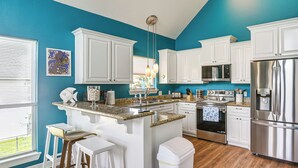 Una cocina con armarios blancos, un refrigerador de acero inoxidable, una encimera de granito y una ventana con persianas.