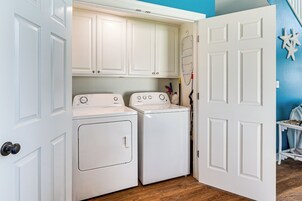 A laundry room with two white washers and dryers, wooden flooring, and a blue wall.